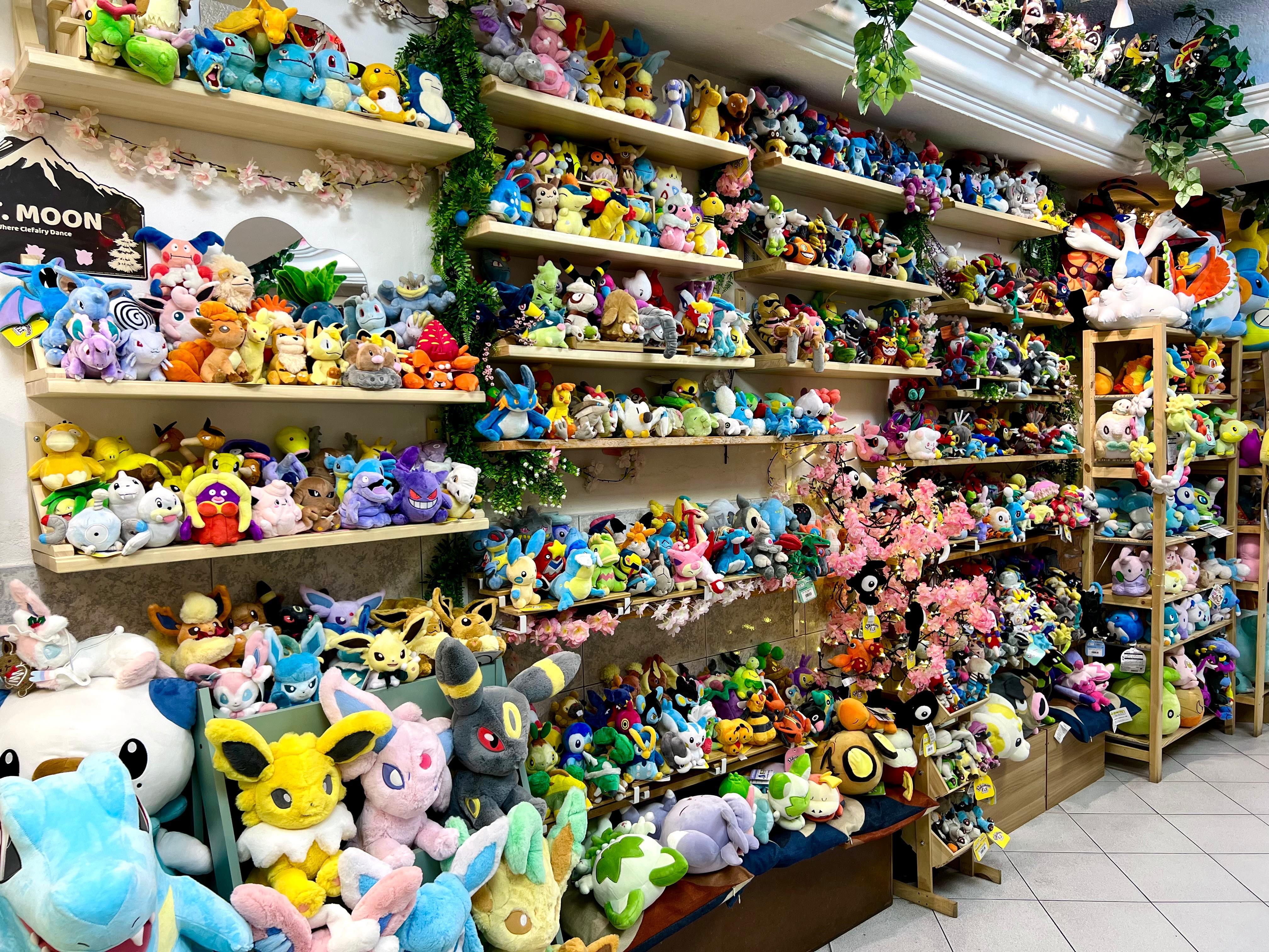 Pared completa de la tienda con cientos de peluches Pokémon organizados en repisas
